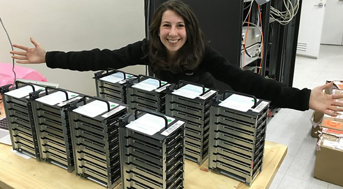 Researcher Katie Bouman (MIT), who led the development of the algorithm to obtain the black hole photo with the EHT, proudly poses with the project's hard disks.
